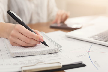 Closeup of woman hand writing notes and using calculator