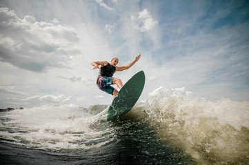 Athletic man wakesurfing on the board against the cloudy sky - obrazy, fototapety, plakaty