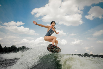 Screaming young woman jumping on the board wakesurfing on the river