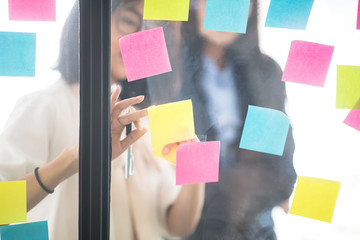 Creative businesspeople putting their ideas at sticky notes on window during a presentation in meeting room. Smiling partners brainstorm concept. Setup studio shooting.
