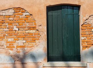 Fototapeta na wymiar Window with green shutters on red brick wall of houses. Italy, Venice, Murano.