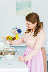 side view of beautiful woman breaking egg for dough in kitchen