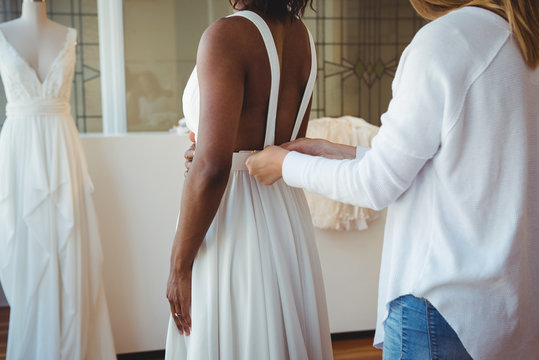 Woman trying on wedding dress with the assistance of fashion designer