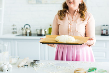 cropped image of woman holding tray with dough for baking bread in kitchen