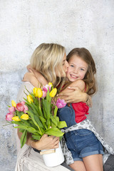 Young and blond and pretty mother gets a bouquet of colorful flowers from her daughter on...