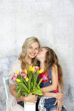 Young and blond and pretty mother gets a bouquet of colorful flowers from her daughter on Mother‘s Day