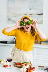 beautiful woman covering eyes with bell peppers at kitchen