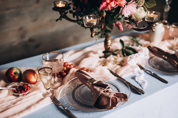 close-up of a glass plate with vintage instruments on a festive table served with a blue tablecloth vintage glasses and flowers with candles on a wooden wall background