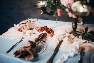 close-up of a glass plate with vintage instruments on a festive table served with a blue tablecloth vintage glasses and flowers with candles on a wooden wall background