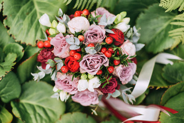 close-up of a wedding bouquet of roses and pions of berries and greens lies in green leaves