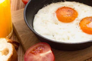 Breakfast with two fried eggs in pan, slice of french bread, tomato, fresh orange juice on mat