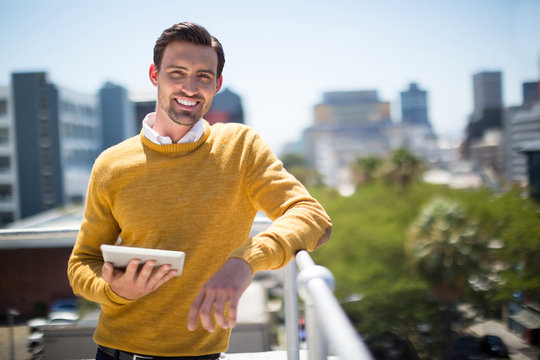 Smiling man standing on balcony with digital tablet