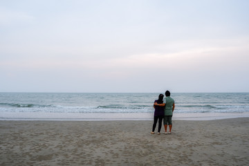 The back of two persons standing on the beach.