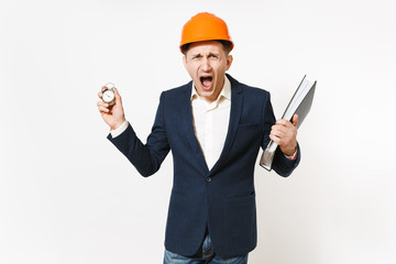 Irritated dissatisfied businessman in dark suit, protective construction helmet screaming and holding folder for papers document and alarm clock isolated on white background. Time is running out.