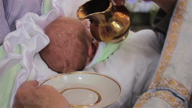 priest pours water on the baby's head,the priest baptizing the baby with water pours his head on sacred water
