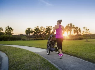 Fotobehang Beautiful, fit women walking and jogging outdoors along a paved sidewalk in a park pushing a stroller at sunset © Brocreative