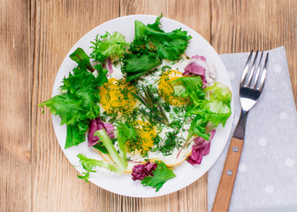 Fried eggs with greens on a plate on a wooden background. Healthy breakfast.