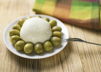 Cheese mozzarella and olives on a plate on a wooden background.