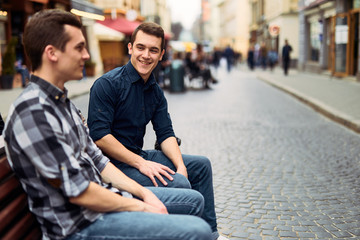 Two man sit on bench and talk on the street
