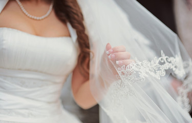 Fine art wedding. Portrait of a young beautiful sexy tender bride in white lace wedding dress gracefully put hand on veil. Veil is thrown over her face. Closeup view. Groom at background