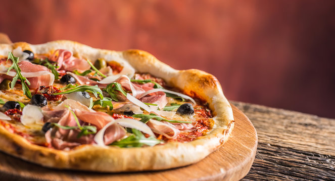 Italian pizza with prosciutto tomatoes olives olive oil parmesan cheese and arugula.
