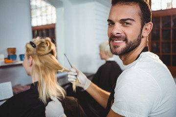 Smiling male hairdresser dyeing hair of her client at a salon