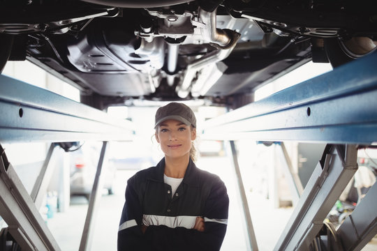 Female mechanic standing with arms crossed under a car