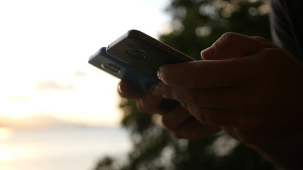 A man is holding two phones in his hands at sunset. hd