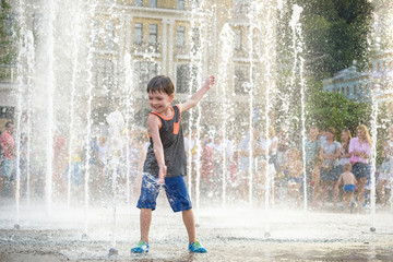 excited boy having fun between water jets, in fountain. Summer in the city