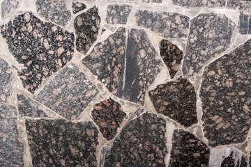 Close-up wall of gray smooth polished granite stones of different form.