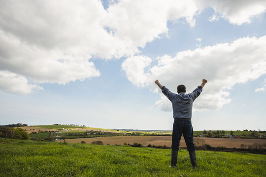 Man standing with arms raised against cloudy sky