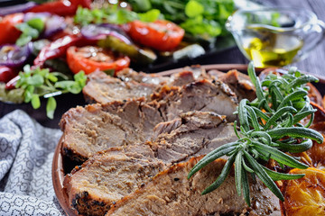 Baked pork with slices of roasted orange, decorated with rosemary, is on a wooden table next to French fries, grilled vegetables, cooked for lunch