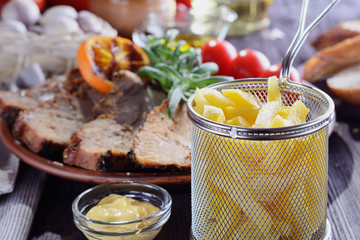 Baked pork with slices of roasted orange, decorated with rosemary, is on a wooden table next to French fries, grilled vegetables, cooked for lunch