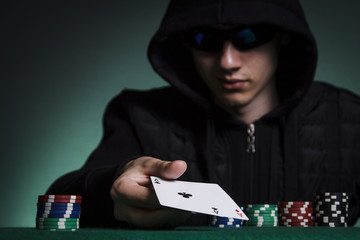 A guy in a black jacket holds a pair of aces against a pile of poker chips
