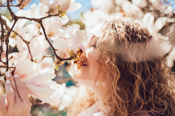 beautiful smiling girl sniffs fragrant magnolia flowers, walks in the park on a warm spring day