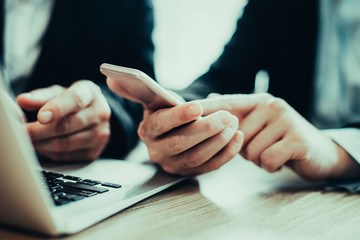 Close-up of hand of businesswoman holding mobile phone and reading message. Male colleague sitting...