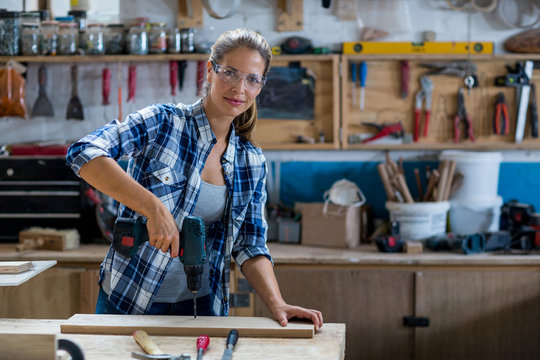 Female carpenter drilling a hole in a wooden plank