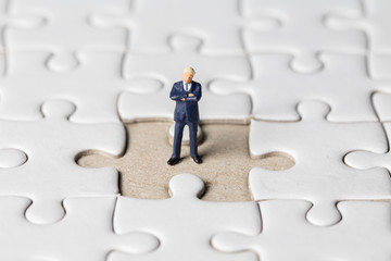 Miniature businessman stand on white jigsaw. One jigsaw are missing from board. Business vision concept.