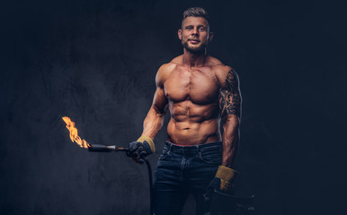 Brutal tattoed male welder with a stylish haircut and beard, with muscular body, dressed in only...