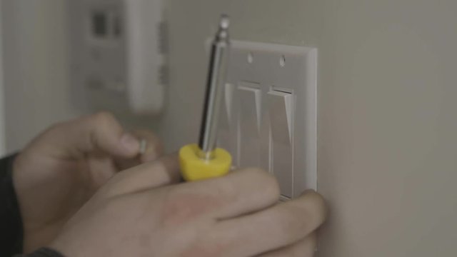 A handyman removes a light switch cover off of the wall.