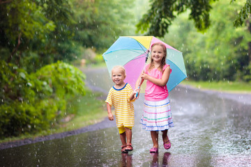 Kid with umbrella playing in summer rain.