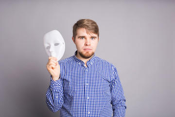 young man taking off plain white mask revealing face, gray background