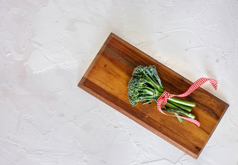 Broccolini on wooden board with red and white squares napkin on grey concret background, top view, copy space