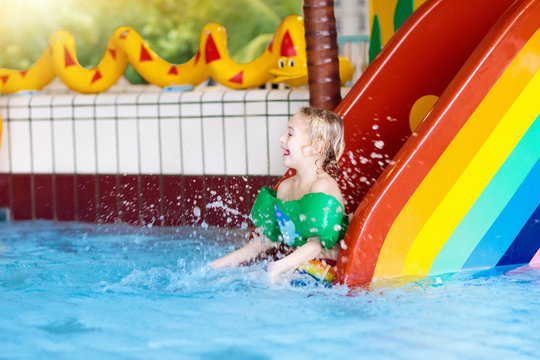 Child on swimming pool slide. Kids swim. Water fun