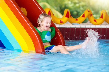 Child on swimming pool slide. Kids swim. Water fun