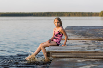 The young girl splashes by his feet in the lake, summer in Finland