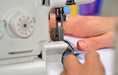 The woman at the sewing machine processes a white fabric, on manufacture close-up of a hand.