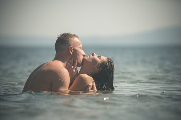 Couple full of desire hugs in sea. Couple in love hugs and kissing in ocean water. Brunette with...