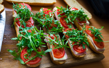 Fresh submarine baguette sandwich with ham, cheese, tomatoes and wild rocket. Selective focus