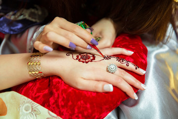 Henna design tattoo. Women applying flowers henna tattoo on women hands. Artist applying henna...